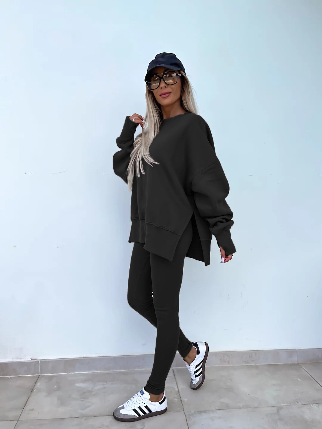 Black round-neck loose sweatshirt with long hip-covering length and side slits at the hem, paired with high-elasticity slim-fit trousers. Leisure suit. Model is wearing and showing the side.
