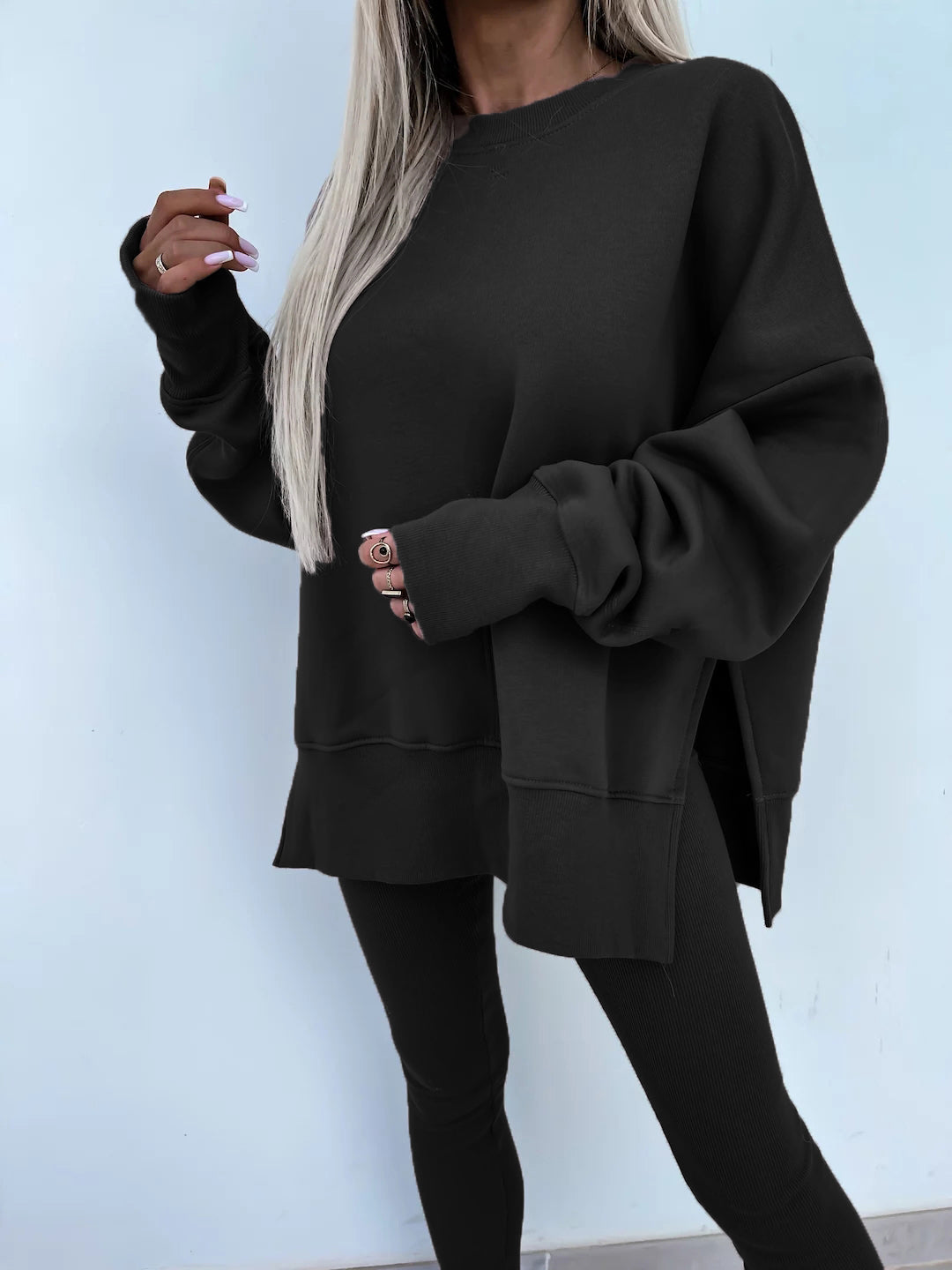 Black round-neck loose sweatshirt with long hip-covering length and side slits at the hem, paired with high-elasticity slim-fit trousers. Leisure suit. Model is wearing and showing the front